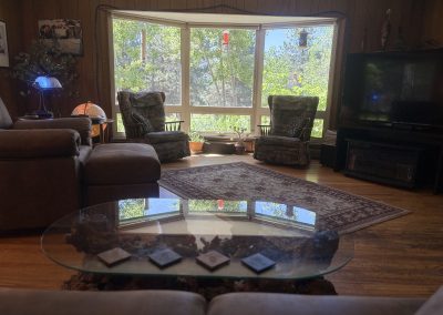 Cozy living room with bay window, comfortable seating, and glass coffee table at Travel Magick Spiritual Retreat Center main house Colorado