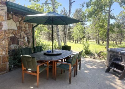 Outdoor patio dining area with BBQ grill, hot tub, and shaded table at Travel Magick Spiritual Retreat Center main house Colorado