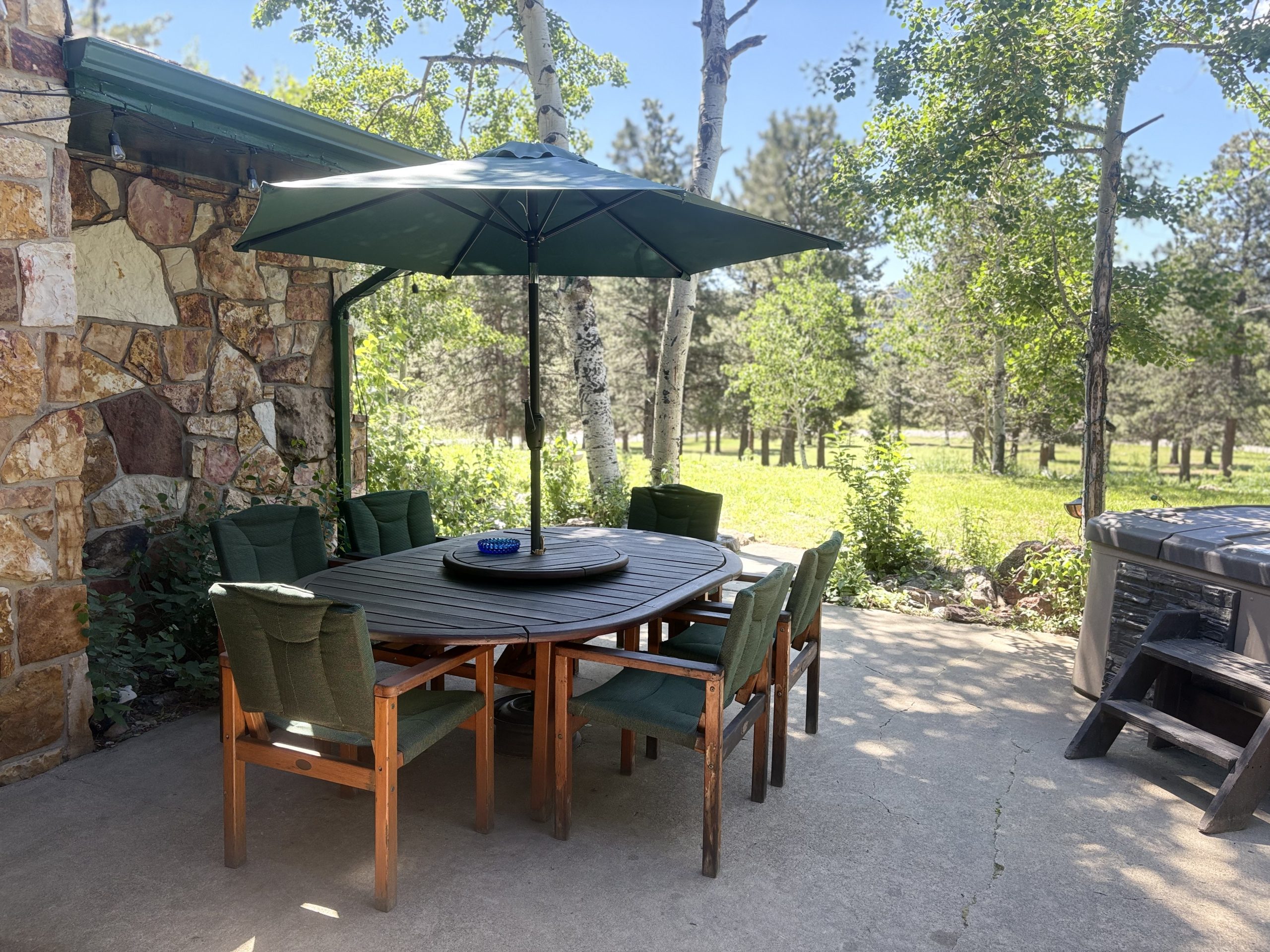 Outdoor patio dining area with BBQ grill, hot tub, and shaded table at Travel Magick Spiritual Retreat Center main house Colorado