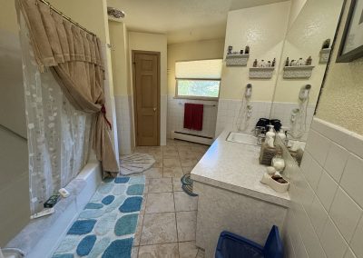 Spacious main house bathroom with bathtub, shower, and blue accent rugs at Travel Magick Spiritual Retreat Center Colorado