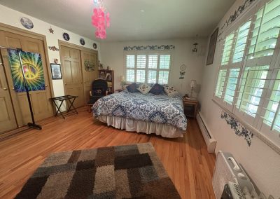 Bright bedroom with blue patterned bedding and multiple windows overlooking gardens at Travel Magick Spiritual Retreat Center main house Colorado