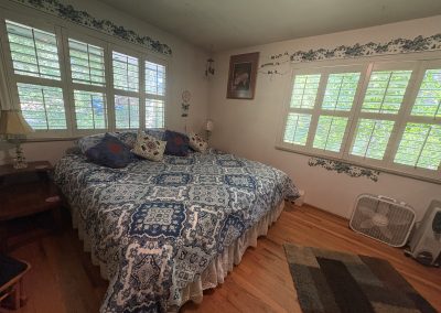 Bright bedroom with blue patterned bedding and multiple windows overlooking gardens at Travel Magick Spiritual Retreat Center main house Colorado