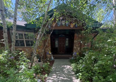 Rustic stone cottage with green metal roof surrounded by lush aspen trees and wildflowers in Colorado Rocky Mountains