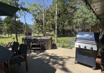 Outdoor patio dining area with BBQ grill, hot tub, and mountain views at Travel Magick Spiritual Retreat Center Colorado main house