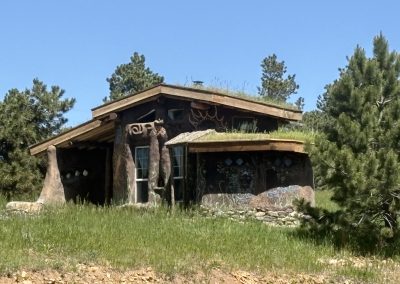 Hand-built earth building with sculptural adobe walls and sacred murals surrounded by stone circle at Travel Magick Spiritual Retreat Center Colorado