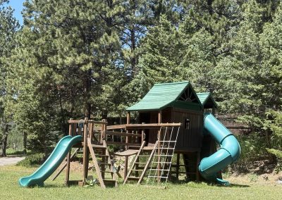 Large wooden playground with slides and climbing structures surrounded by pine trees at Travel Magick Spiritual Retreat Center Colorado