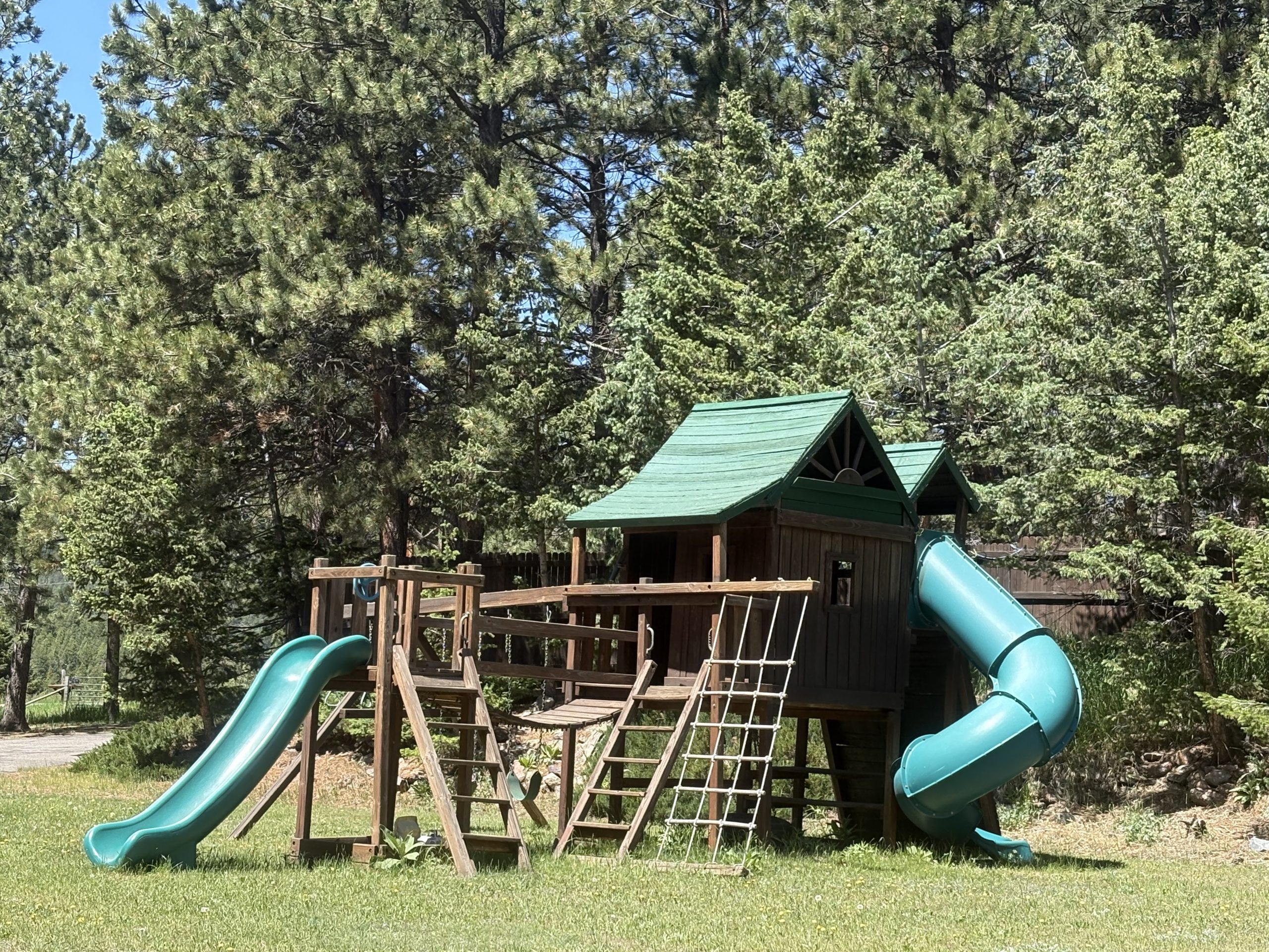 Large wooden playground with slides and climbing structures surrounded by pine trees at Travel Magick Spiritual Retreat Center Colorado