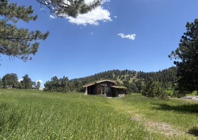 Hand-built earth building with sculptural adobe walls and sacred murals surrounded by stone circle at Travel Magick Spiritual Retreat Center Colorado