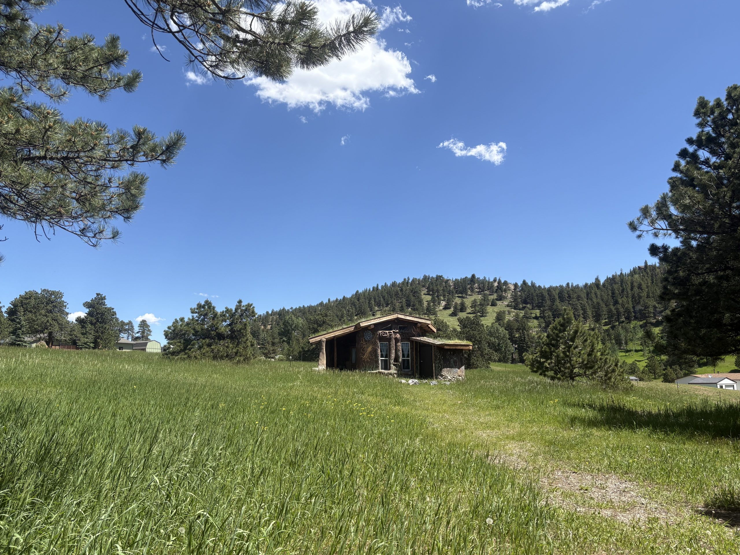 Hand-built earth building with sculptural adobe walls and sacred murals surrounded by stone circle at Travel Magick Spiritual Retreat Center Colorado