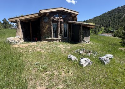 Hand-built earth building with sculptural adobe walls and sacred murals surrounded by stone circle at Travel Magick Spiritual Retreat Center Colorado