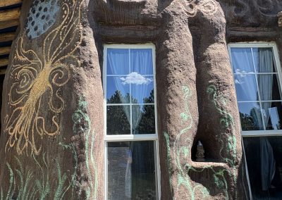 Hand-built earth building with sculptural adobe walls and sacred murals surrounded by stone circle at Travel Magick Spiritual Retreat Center Colorado