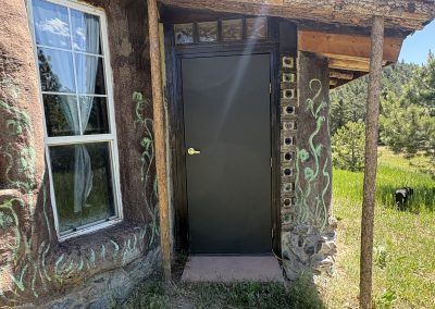 Exterior entrance of hand-built earth building with sacred murals and glass bottle details at Travel Magick Spiritual Retreat Center Colorado