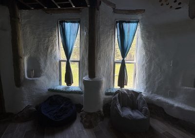Built-in adobe seating nooks with windows and blue curtains in hand-built earth building at Travel Magick Spiritual Retreat Center