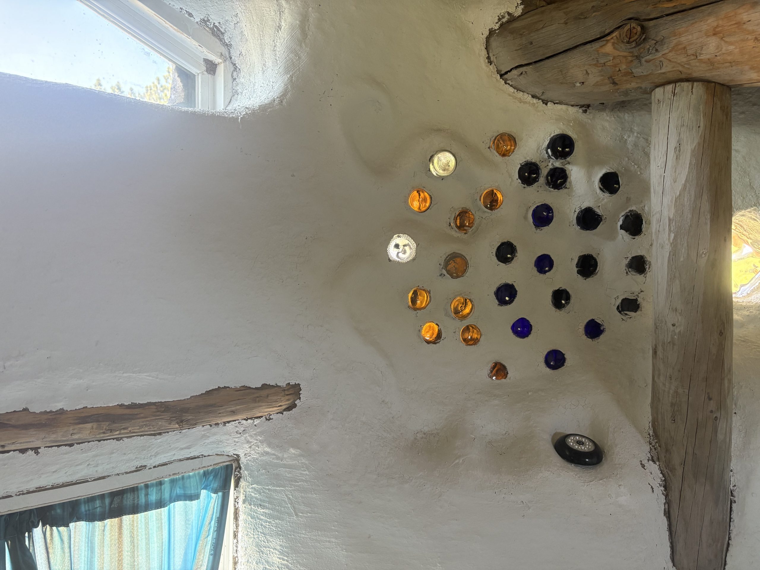 Artistic glass bottle wall installation with colorful amber and blue bottles in hand-built earth building at Travel Magick Spiritual Retreat Center
