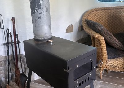 Wood burning stove with chimney pipe and wicker chair inside hand-built earth building at Travel Magick Spiritual Retreat Center
