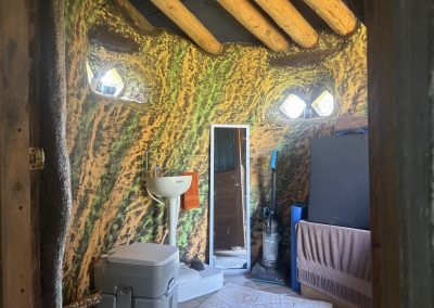 Interior of hand-built earth building bathroom with curved adobe walls and natural light windows at Travel Magick Spiritual Retreat Center