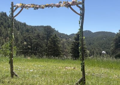 Rustic wooden arbor with flower decorations overlooking mountain meadow at Travel Magick Spiritual Retreat Center Colorado