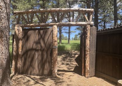 Rustic wooden gateway entrance with natural log pergola leading to meadow at Travel Magick Spiritual Retreat Center Colorado